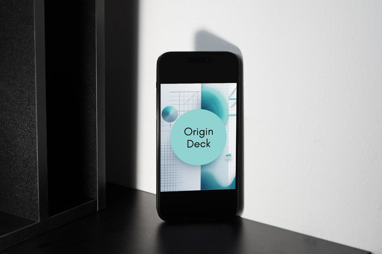 A black smartphone stands upright on a dark surface against a white wall, displaying a game card or app graphic with the text 'Origin Deck' in a light blue circle.