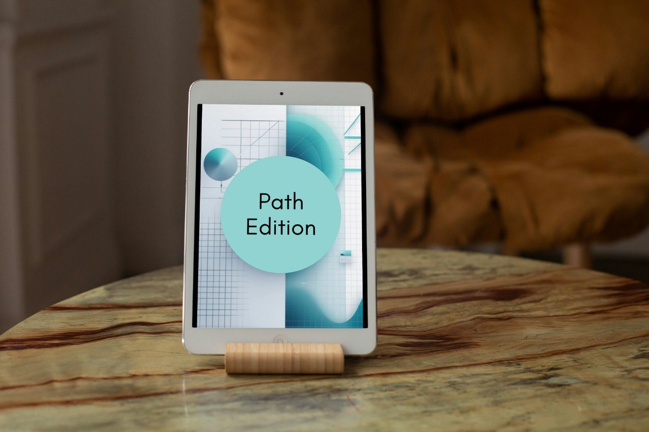 A tablet device on a small wooden stand displaying a cover titled 'Path Edition' in a home setting with a marble table and a brown leather armchair in the background.