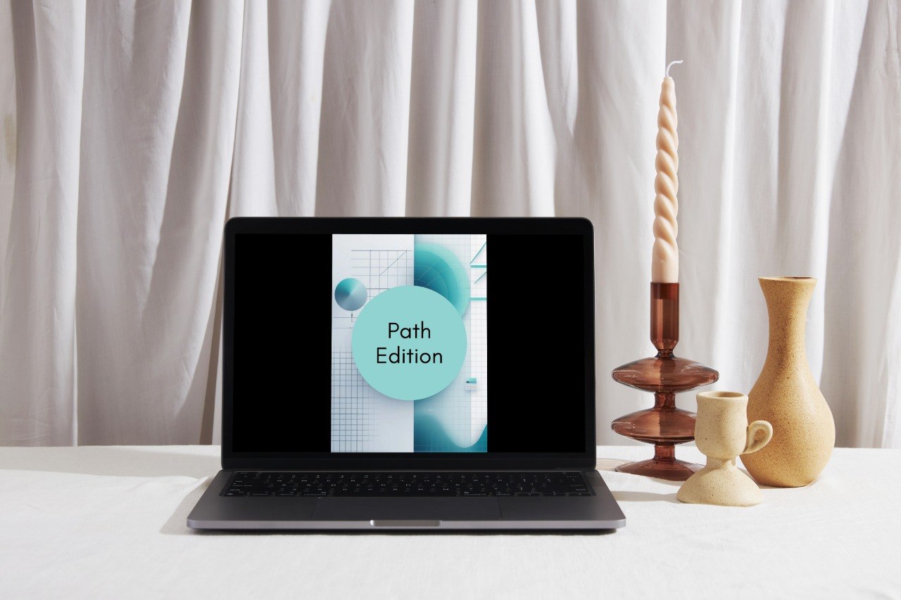 A laptop displaying a graphic with the text 'Path Edition' sits on a white tablecloth in front of white draped curtains, styled with a tall spiral candle, ceramic cups, and a vase on the right.